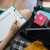Traveller writing an air travel checklist next to packed suitcase